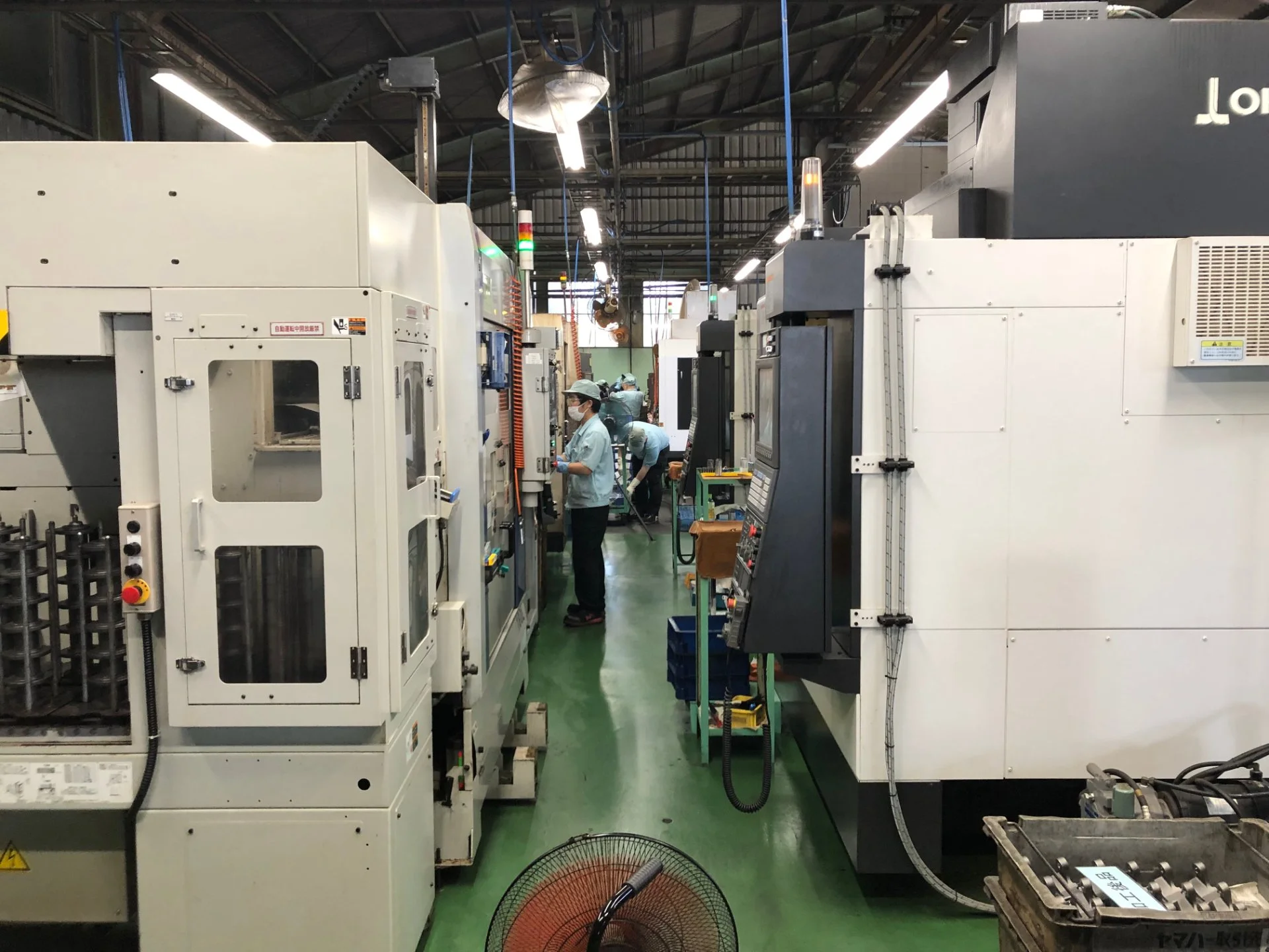 加工設備が並ぶ工場内の通路で、作業者が機械を操作している様子