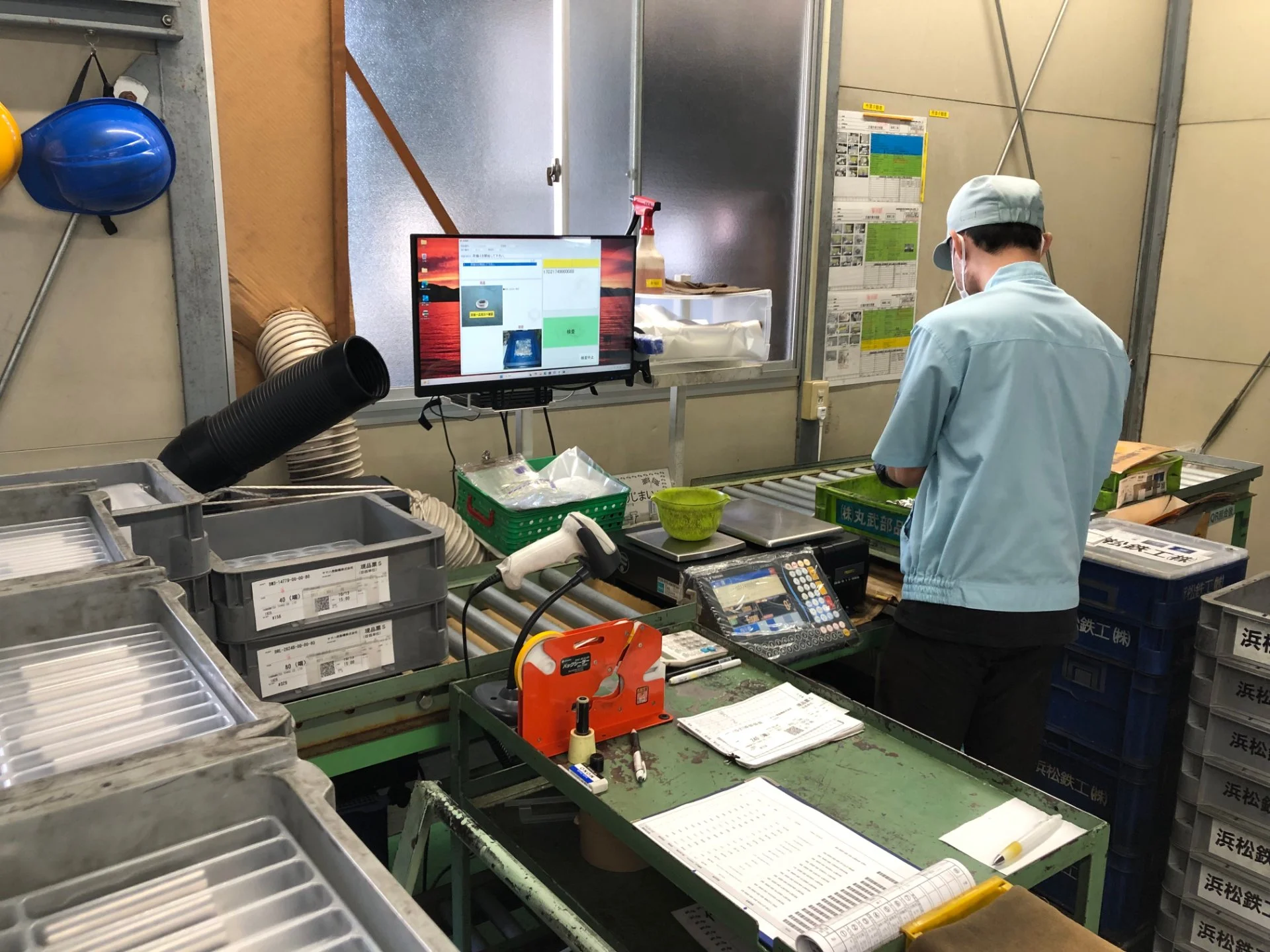 検品用のモニターや計量機を備えた作業台で、製品を確認する作業者